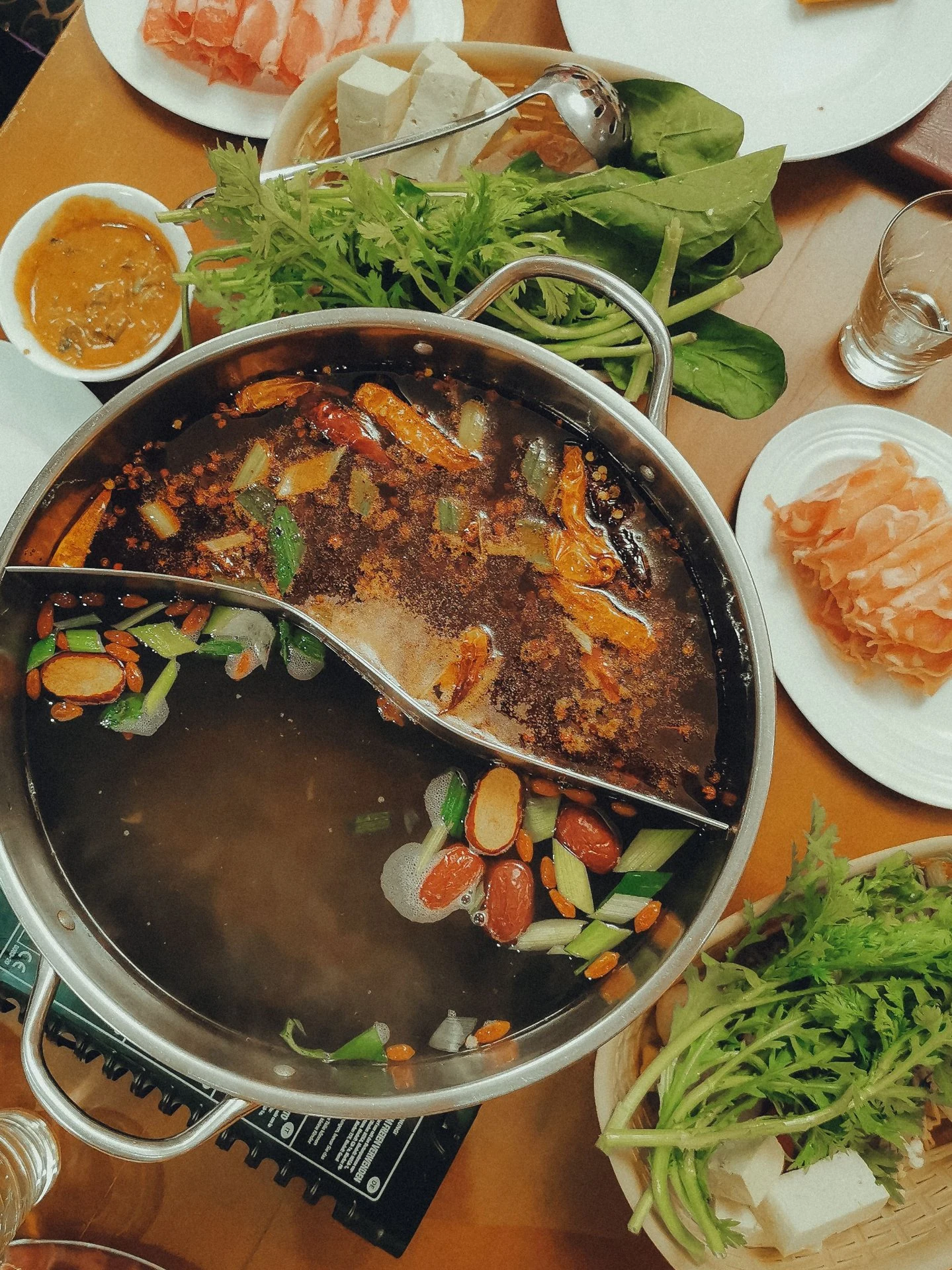 A split hotpot with spicy and mild broth, surrounded by fresh ingredients