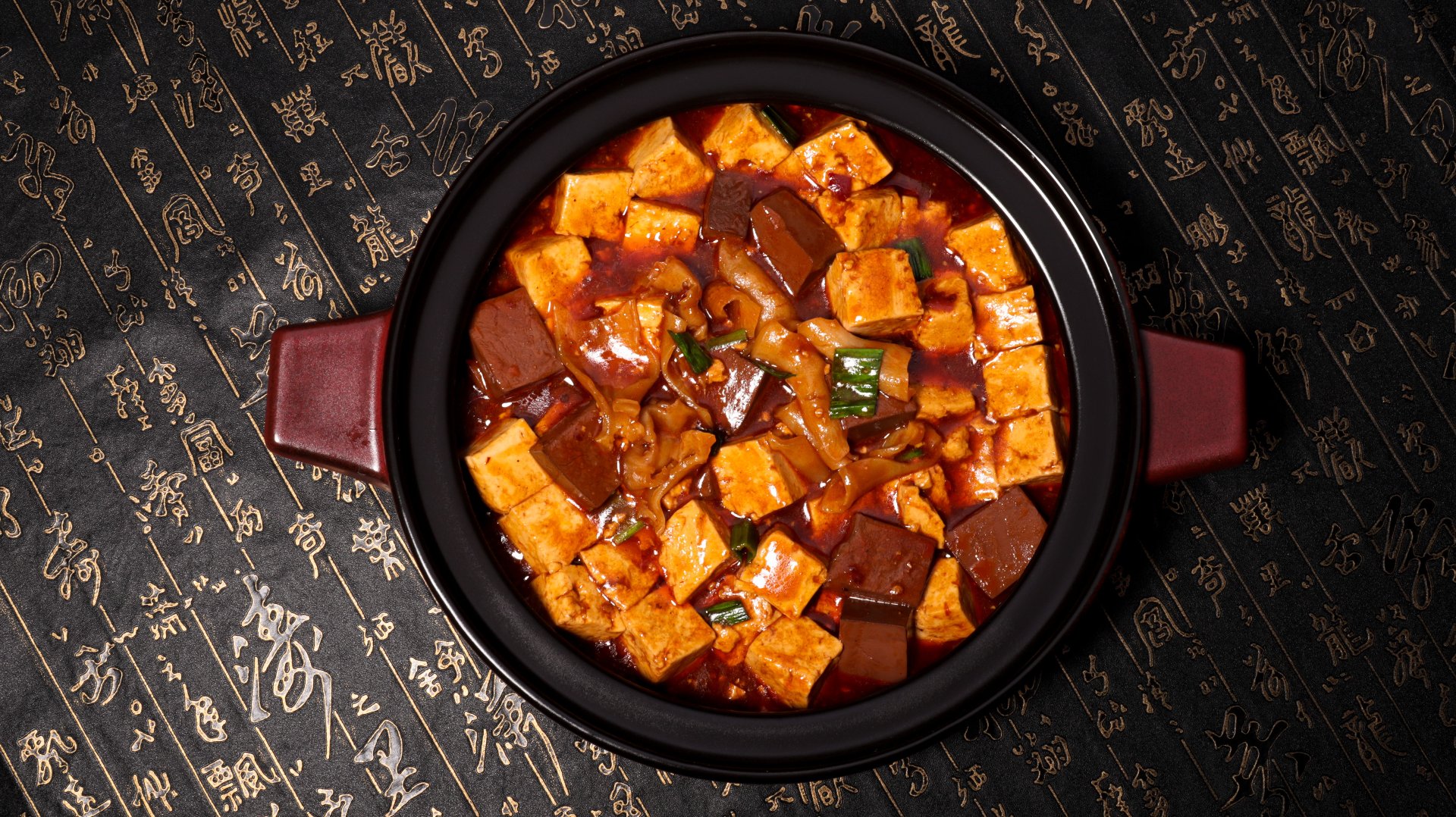 Mapo tofu (麻婆豆腐) — Sichuan's iconic dish of silky tofu in a fiery chili-and-Sichuan-peppercorn sauce, served in a traditional clay pot on a calligraphy tablecloth