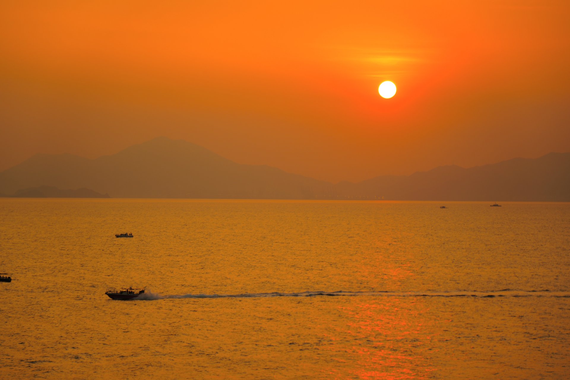 Golden sunset over the East China Sea with a small fishing boat in the foreground and a mountain range silhouetted on the horizon