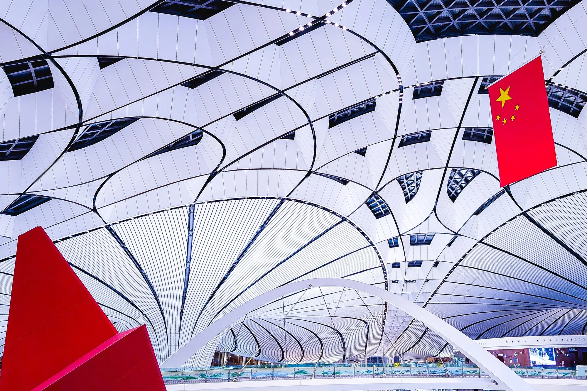 The bright interior of a major Chinese airport terminal under a curved ceiling with the Chinese national flag