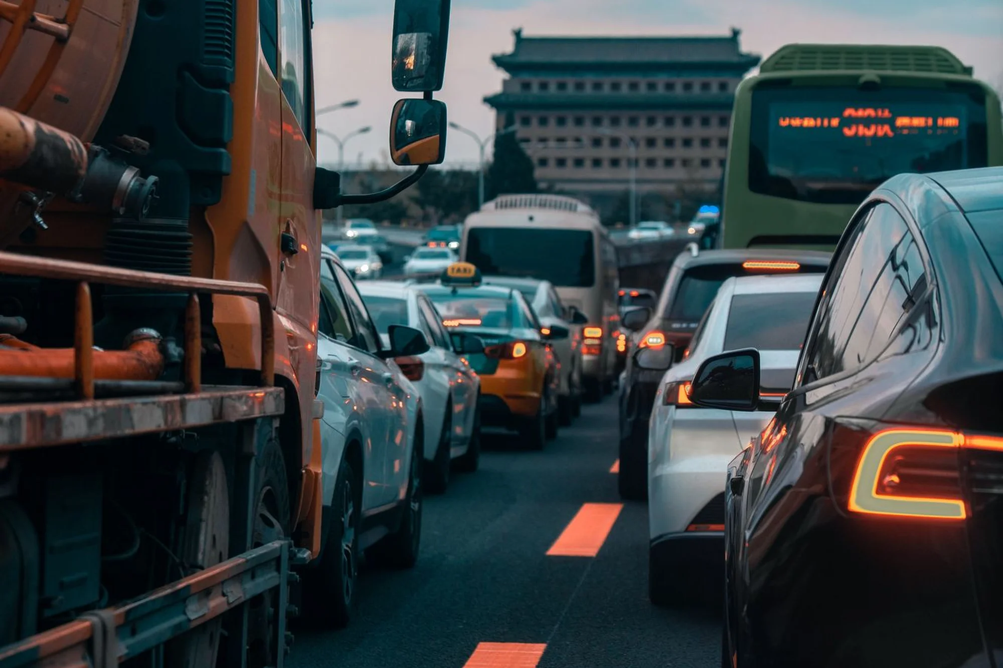 Evening traffic on a multi-lane road in Beijing with a historic city gate in the distance