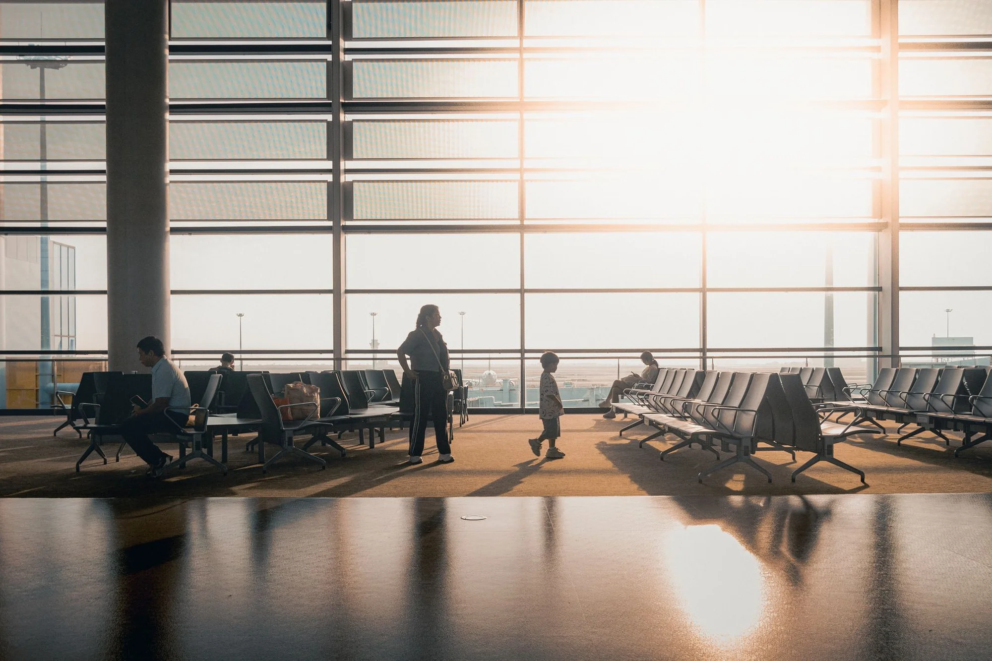 Silhouettes of travellers in a sunlit Shanghai airport departure hall with rows of empty seats