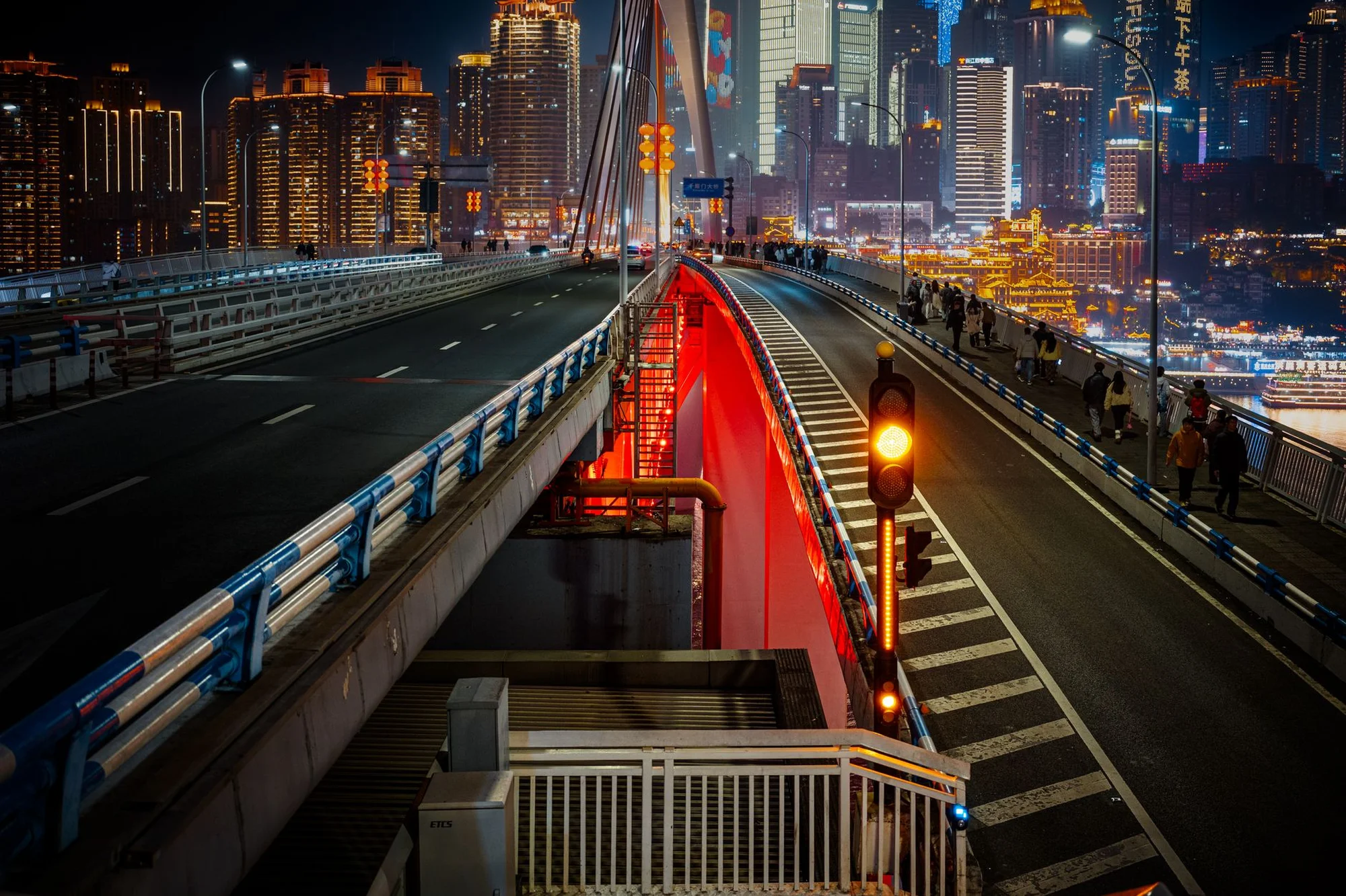 A wide city street in a Chinese metropolis at dusk, with lit shopfronts and passing traffic