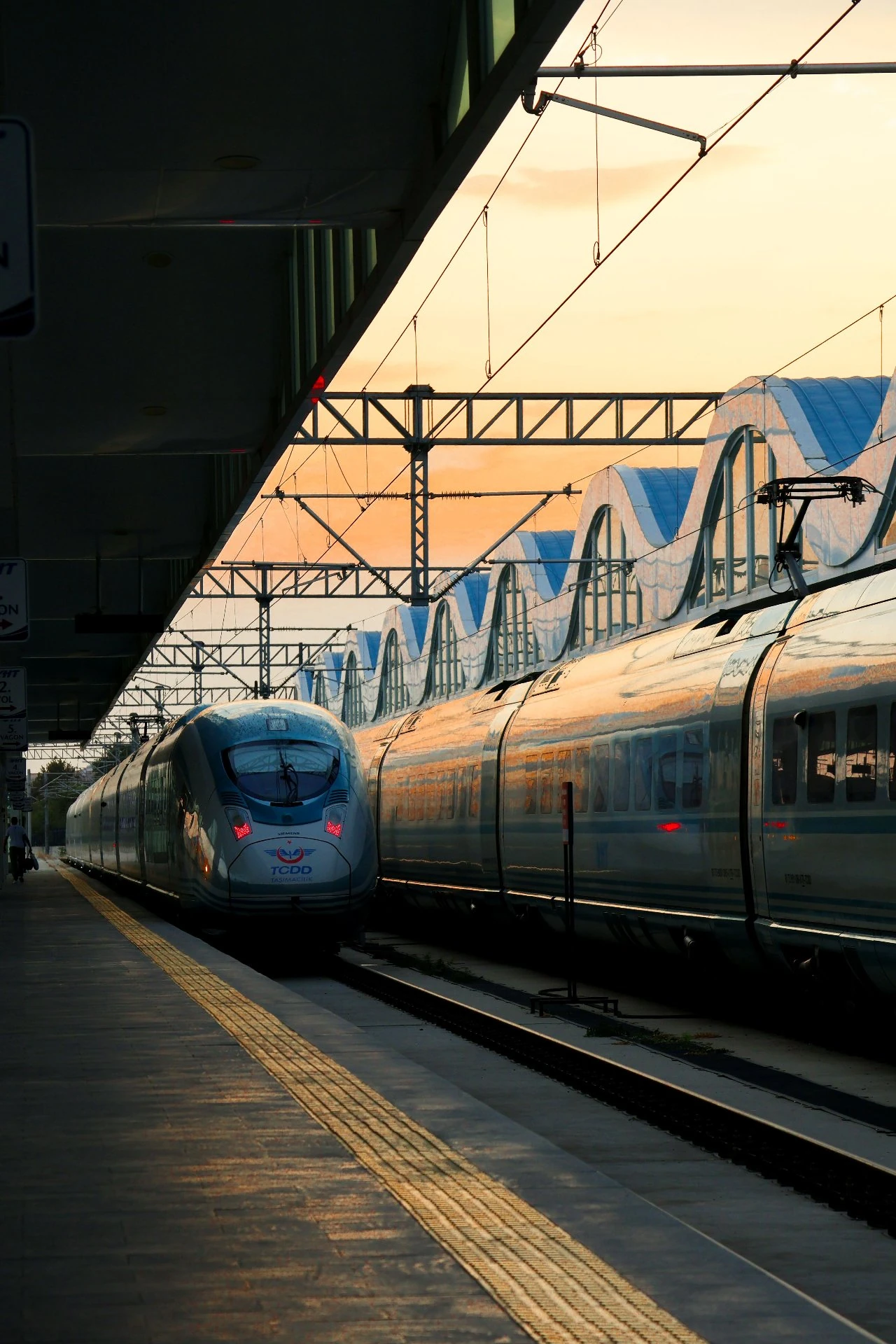 A modern high-speed train waits at a covered platform in warm evening light