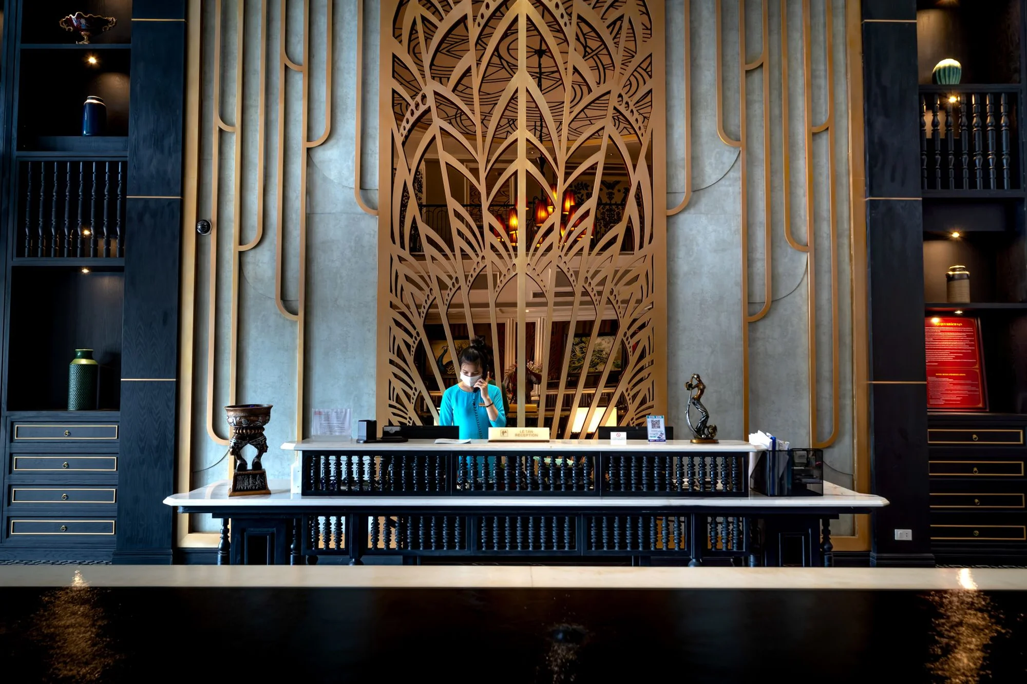 An ornate Asian hotel reception desk with a decorative bronze screen and no documents on the counter