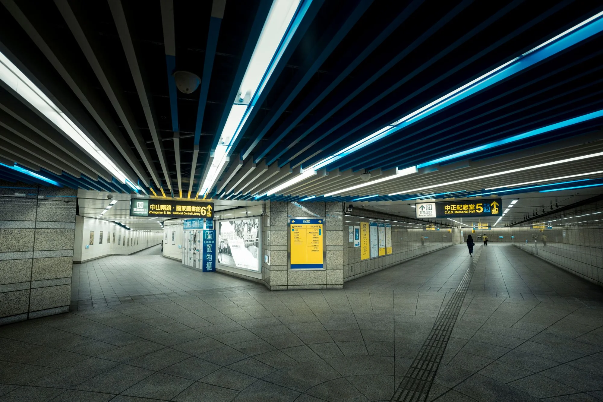 A modern Chinese subway station concourse with yellow directional signs hanging from a curved ceiling