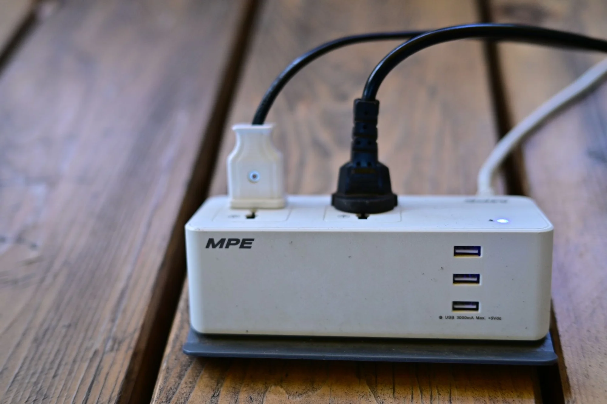 A universal power strip on a wooden table with two plugs and three USB ports