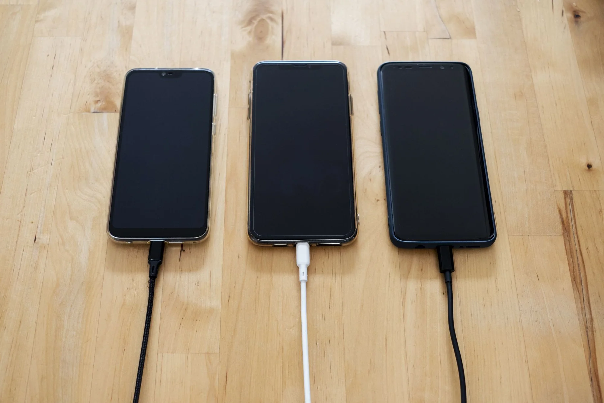 Three smartphones laid out charging with cables on a wooden surface