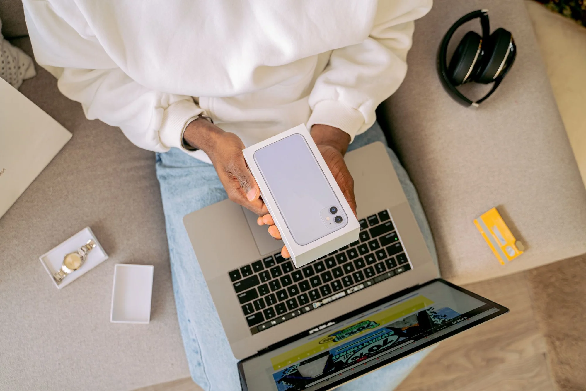 A person on a couch with a smartphone, laptop and credit card for online shopping
