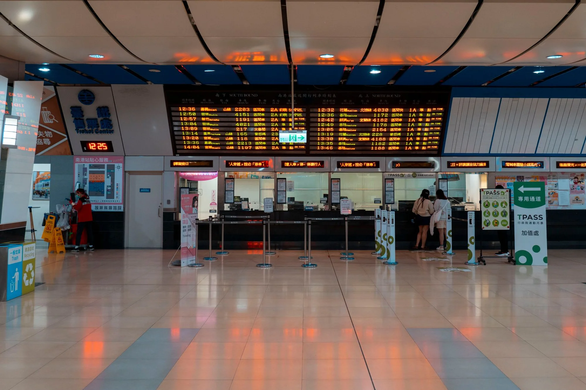 A modern Chinese service hall with numbered counters, a digital timetable and queue rails, where staff help visitors in person