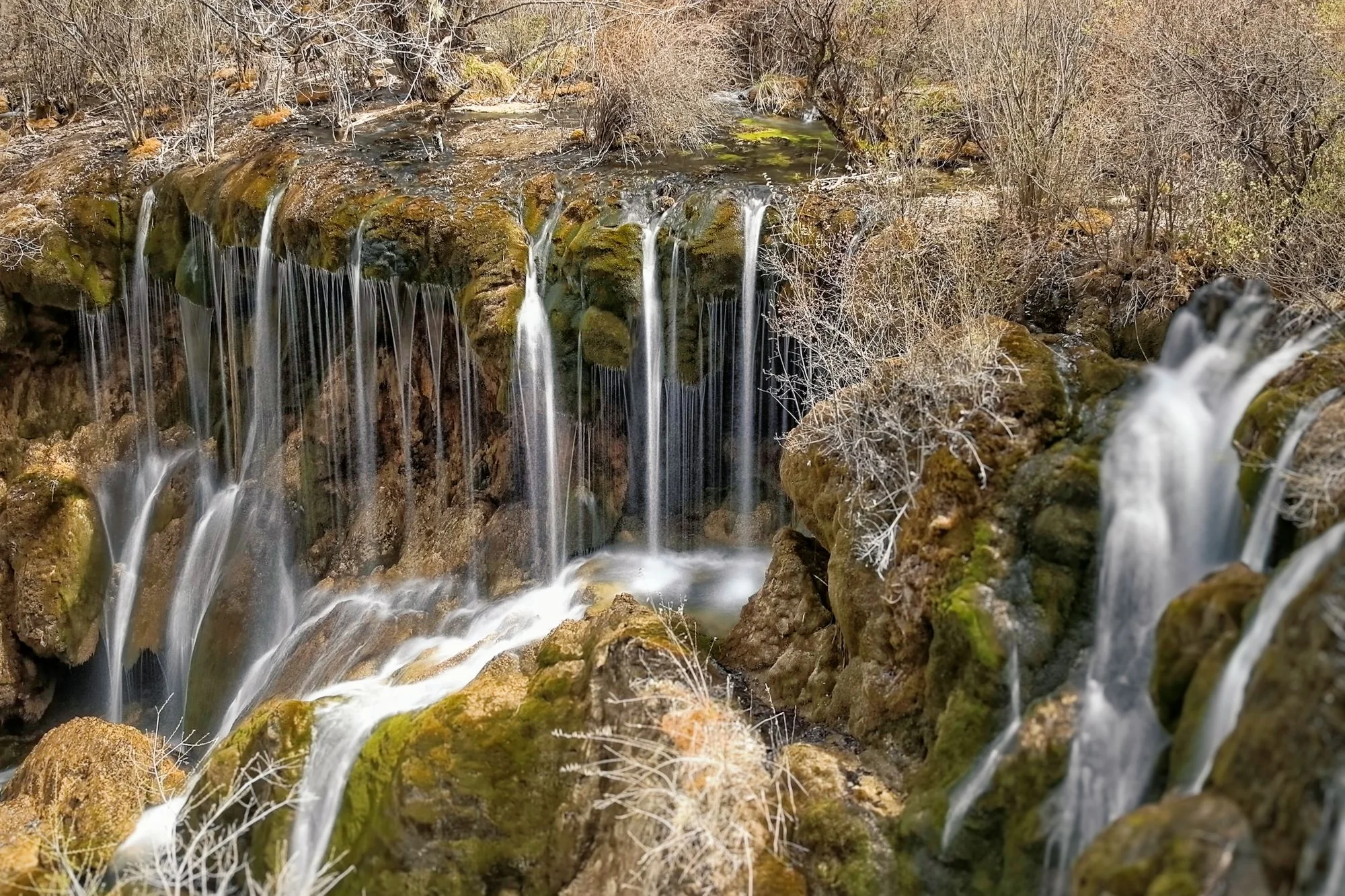 A wide travertine waterfall spilling over mossy terraces in Jiuzhaigou Valley