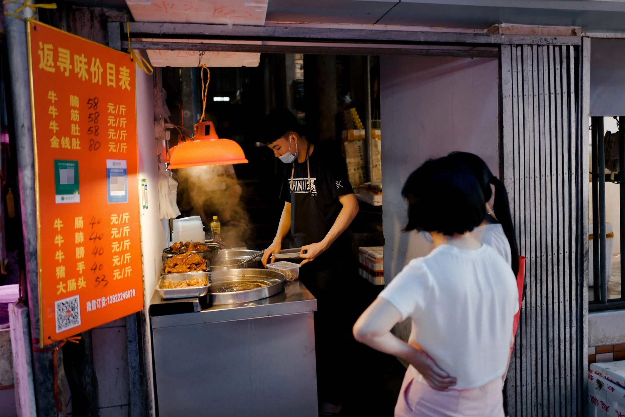 A Chinese street food stall with a WeChat Pay QR code on a red price board