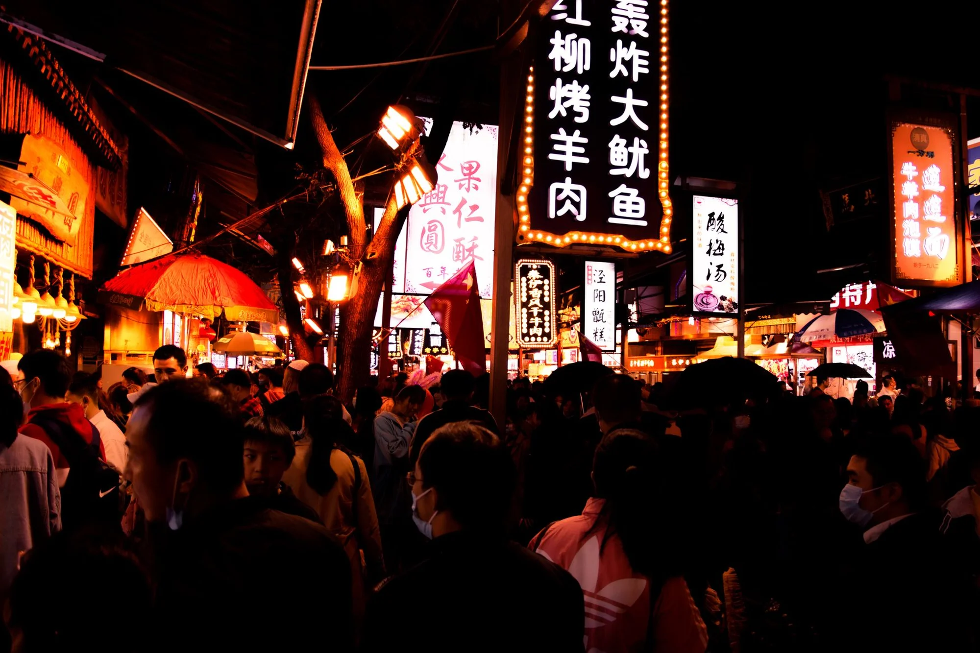 A busy night scene in Xi'an's Muslim Quarter with bright Chinese food signs and crowds