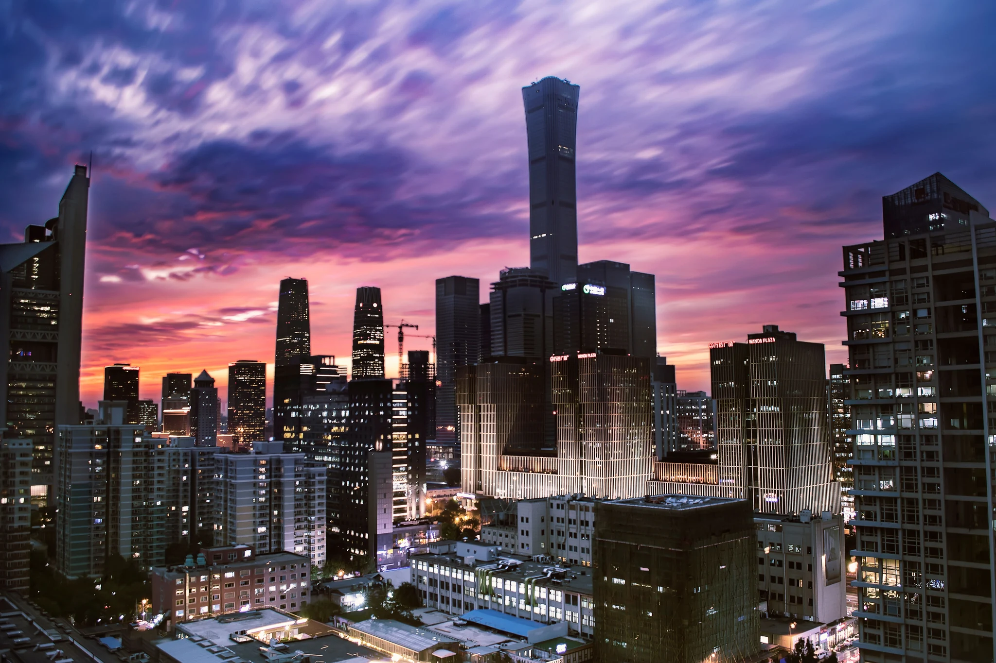 Beijing's Guomao CBD skyline at sunset, with the China Zun tower rising above neighboring skyscrapers under a violet and orange sky