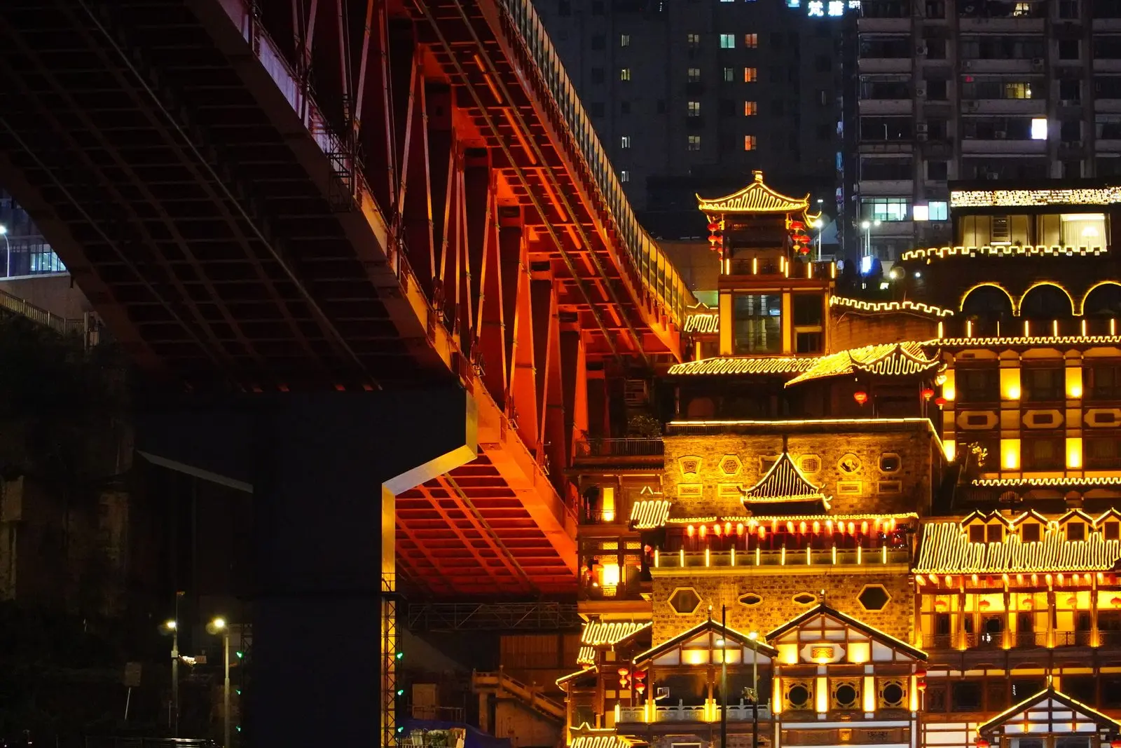 Hongyadong traditional stilted buildings lit up at night beneath a red bridge in Chongqing.