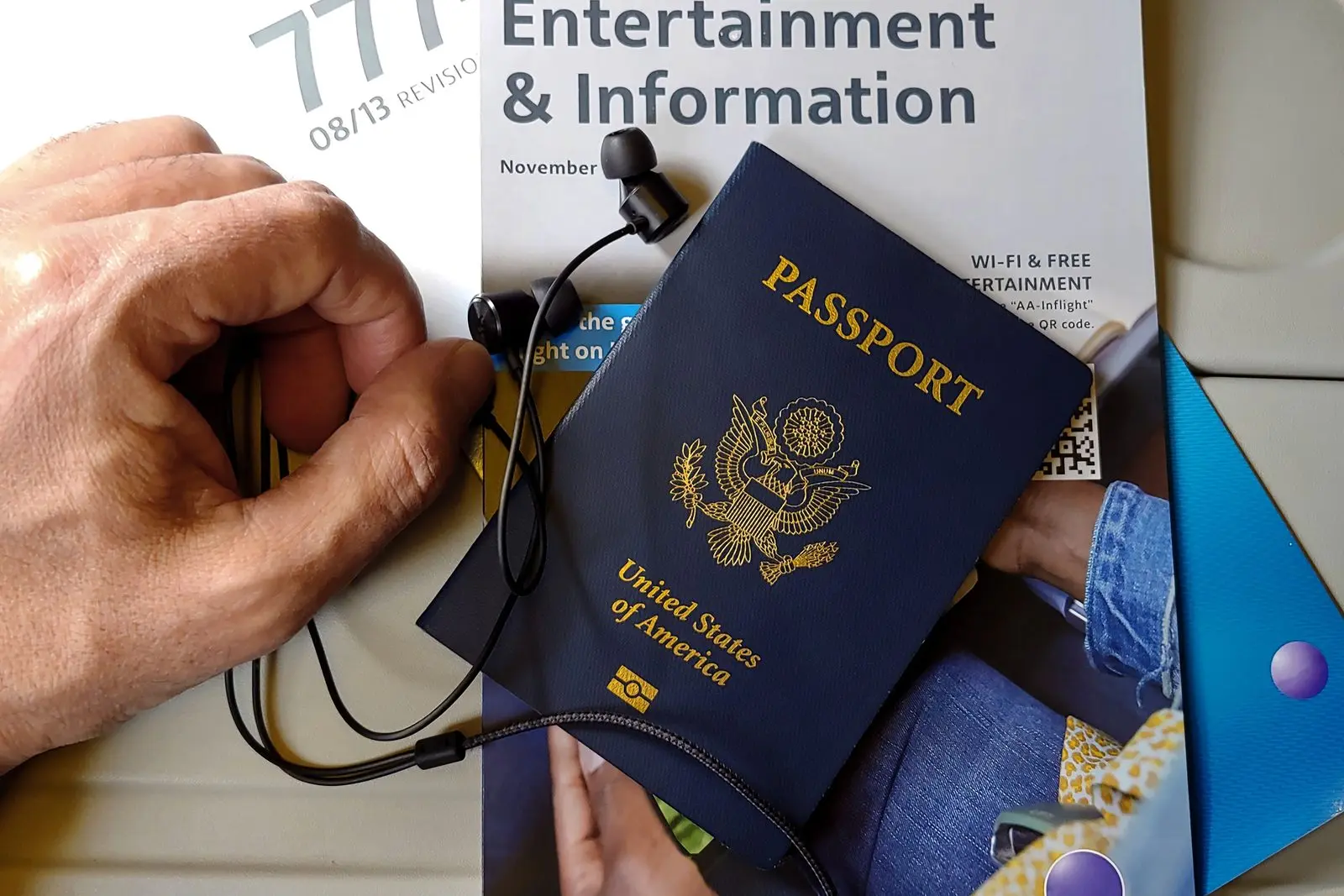 A hand holding a United States passport over an in-flight magazine and entertainment screen.
