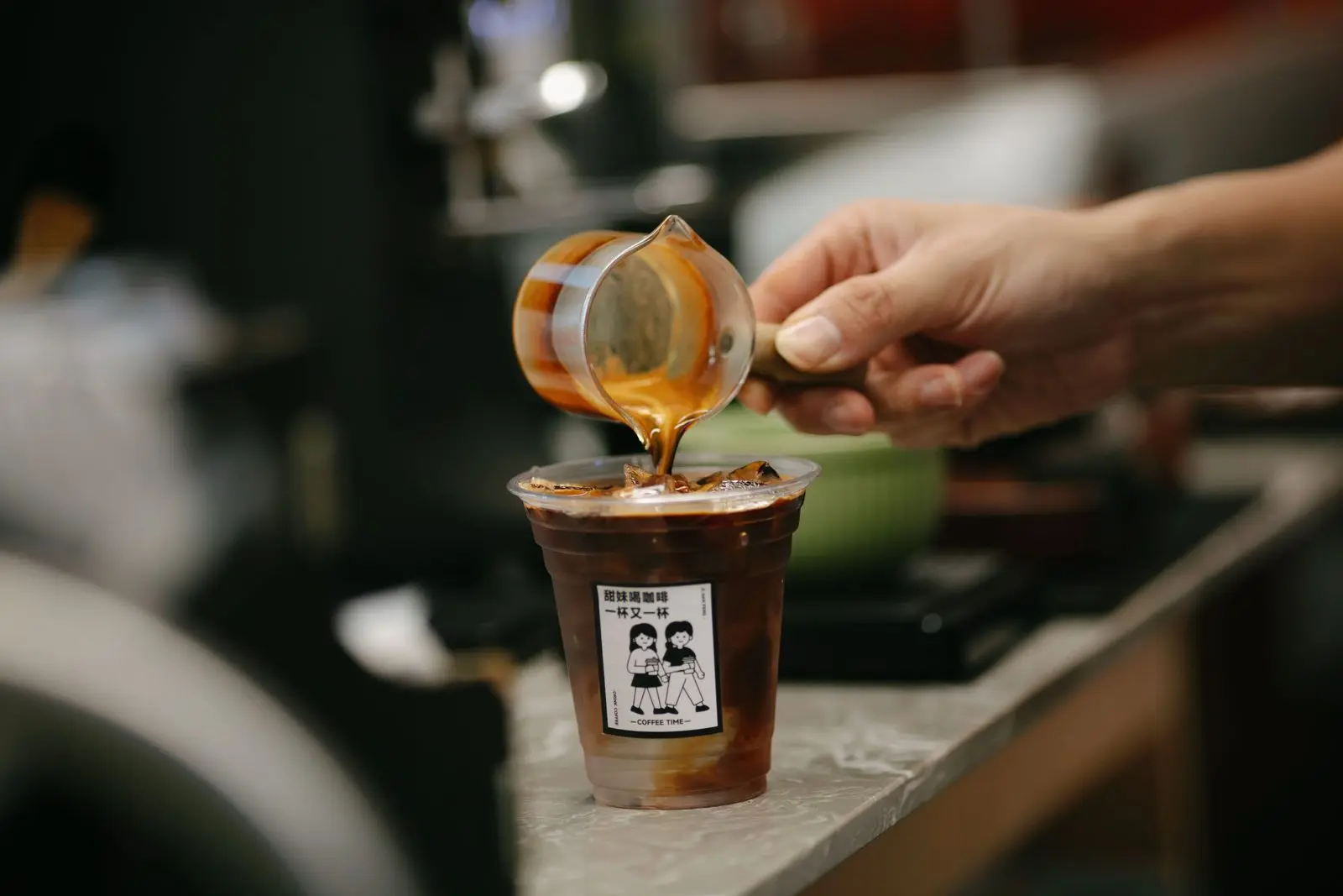 A barista pours iced coffee into a plastic cup with a Chinese-language sticker.