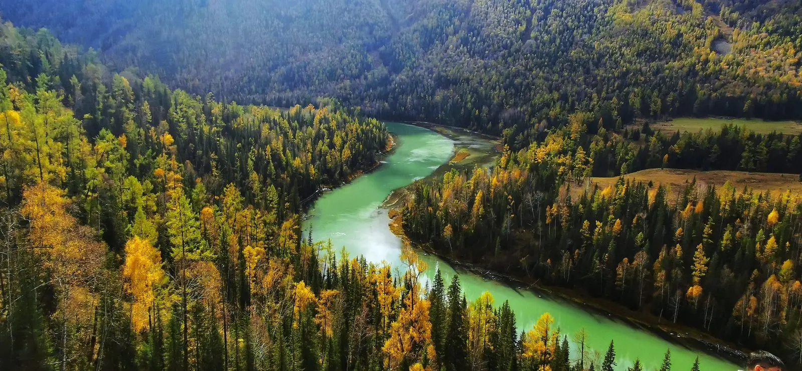 A turquoise river winding through a forested valley in autumn colors.